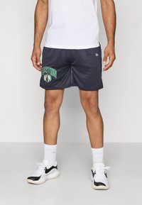 Grå sportsshorts med "BOSTON" grafik i grøn, der har et basketball-logo. Sammen med hvide ankelsokker og sorte/hvide sneakers.