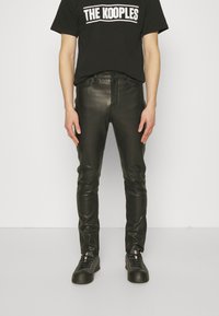 Svarta läderbyxor med slim fit, med en slät yta och klassisk femfickdesign. Matchas med en svart t-shirt med logotyp och sneakers.