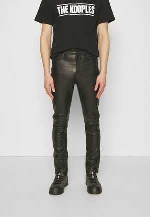 Pantalones de cuero negro con un ajuste slim, que presentan una textura suave y un diseño clásico de cinco bolsillos. Combinados con una camiseta negra con logo y zapatillas.