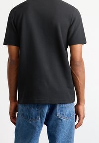 Svart kortärmad skjorta med en texturerad mönster, tillverkad av mjukt tyg. Bärs tillsammans med blå denimjeans med bakfickor och blekt mönster.