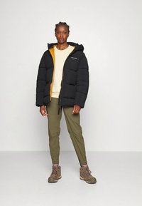 Μαύρο φουσκωτό μπουφάν με πορτοκαλί εσωτερική επένδυση, επενδυμένο σχέδιο, κλείσιμο με φερμουάρ και κουκούλα. Συνδυασμένο με παντελόνι ελιάς και καφέ ορειβατικά μποτάκια.