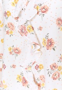 Tissu floral blanc à pois pêche. Il présente des bords volantés et un motif de fleurs jaunes et roses avec des feuilles vertes.