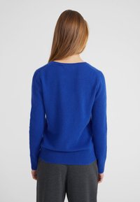 Maglione blu lavorato a maglia con scollatura rotonda, maniche lunghe e polsini a coste. Il tessuto appare morbido con una texture leggermente pelosa.