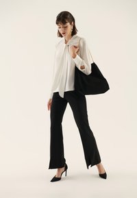 White blouse with a tied neck detail, black flared pants with side slits, and black high-heeled shoes. Black suede handbag with gold chain strap.