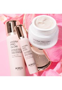 Cuidado hidratante de KIKO Milano: crema Hydra Pro Glow, sérum Hydra Pro Eyes y hidratante de día Hydra Pro abierto con fondo de pétalos de rosa rosa.