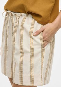 Pantalones cortos de algodón con cintura elástica y cordón. Presentan rayas marrones verticales sobre un fondo beige claro. Incluyen bolsillos laterales.
