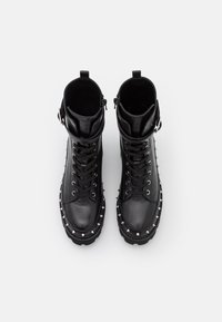 Paire de bottes en cuir noir à lacets avec brides à la cheville et pointes argentées autour de la semelle sur fond blanc.
