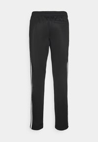 Pantalones deportivos negros de tela suave con una cintura elástica y franjas blancas a lo largo de la longitud de cada pierna.