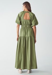 Abito lungo verde oliva con vita arricciata, maniche a sbuffo e dettaglio a fessura sul retro, realizzato in tessuto leggero.