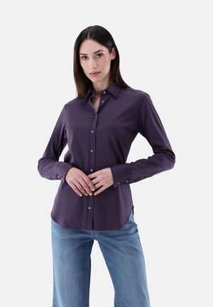 Camicia a maniche lunghe, con bottoni, in tessuto viola intenso. Presenta un colletto classico, una vestibilità sagomata e orlo arrotondato. Abbinata a jeans blu chiaro.