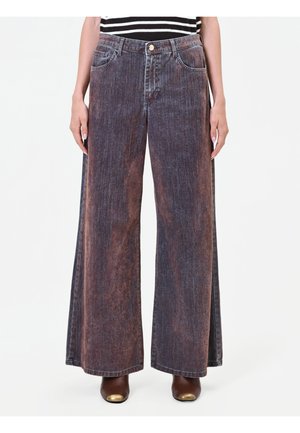 Donna che indossa jeans neri e marroni sbiaditi, a vita alta e gamba larga, con tasche anteriori, abbinati a stivali marroni con punta dorata.