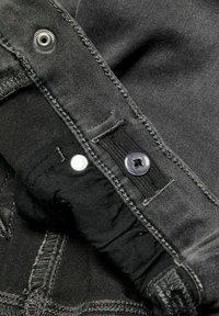 Svart denimtyg med sömdetaljer, en silvertryckknapp och en mörk knäppning med ett elastiskt band.