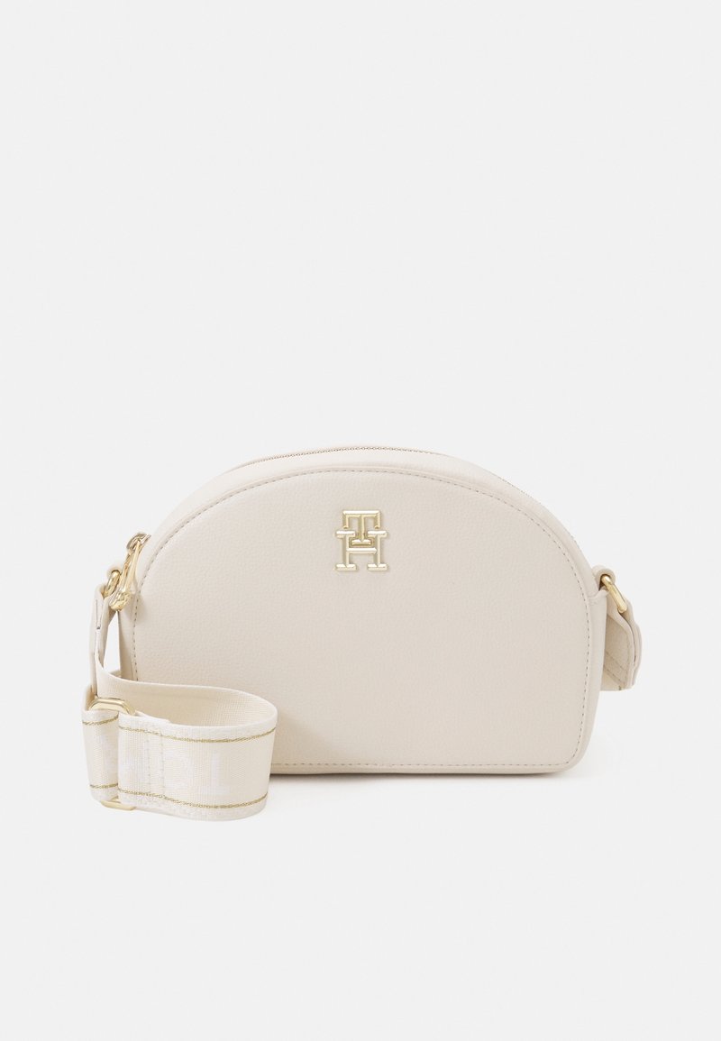 Beige läder crossbody-väska med rundad topp, guldfärgade detaljer och logotyp. Har en avtagbar rem och texturerad yta.