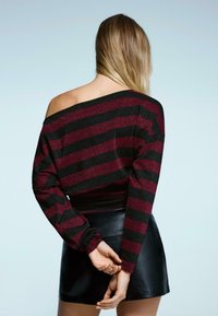 Hosszú ujjú, vállakat szabadon hagyó felső bordó és fekete csíkokkal, csillogó textúrával, fényes fekete bőr szoknyával párosítva.