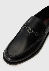 Sorte skinn loafers med en glatt finish, som har en sølvfarget metall «HUGO» logo aksent og detaljert søm langs kantene.