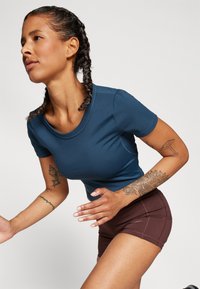 Top azul-marinho de manga curta com decote redondo e design ajustado, emparelhado com calções de atletismo castanhos com detalhes em costura e um corte justo.