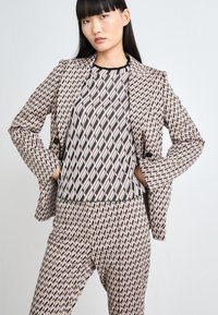 Gemusterter Anzug mit einem Blazer und taillierten Hosen in verschiedenen Schattierungen von Pink, Schwarz und Creme. Der Stoff hat ein geometrisches Diamantmuster.