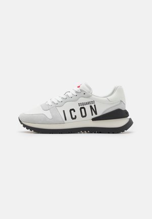 Sneakerit, jotka on valmistettu valkoisesta nahasta ja harmaasta mokasta, mustalla "ICON"-logolla, valkoisilla nauhoilla ja mustalla kumipohjalla.