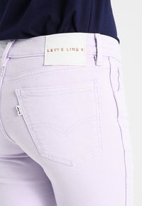 Jeans de mezclilla de color púrpura claro con bolsillos traseros, una etiqueta blanca con letras rojas y un diseño clásico de mezclilla.