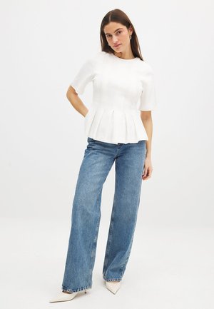 Vit peplum-topp med korta ärmar, texturerad tyg, kombinerad med ljusblå vida jeans och spetsiga beige klackar. Enkelt, rent design.