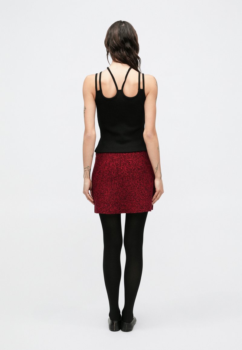 Black sleeveless top with a back design, red textured mini skirt, black tights, and black shoes, viewed from the back.