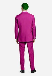 Magenta-Anzug mit schmaler Passform, ausgestattet mit einem Schlitz, passenden Hosen und schwarzen Schuhen. Glatte Textur und maßgeschneiderte Verarbeitung.
