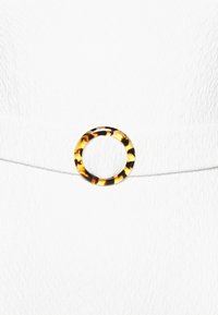 Cuir blanc texturé avec un accent circulaire en écaille de tortue bien en vue. Le design présente une finition lisse et des détails de couture subtils.