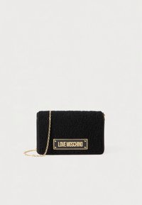 Black textured fabric bag with a gold chain strap, featuring a gold logo plate. Rectangular shape with a zip closure.