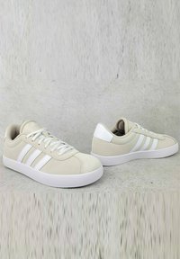 Sneakers beige basse con tre strisce bianche, materiale in tela, punta tonda, suola piatta e colletto imbottito. Design minimalista con lacci.