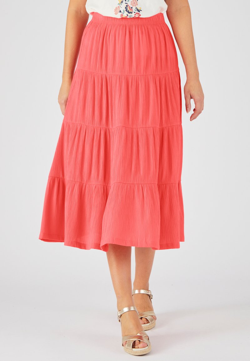Jupe maxi corail à volants en tissu texturé, taille élastique et silhouette évasée, associée à des sandales métalliques à lanières.