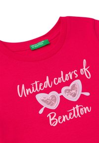 Růžové bavlněné tričko s kulatým výstřihem, na kterém je nápis "United Colors of Benetton" a grafika brýlí ve tvaru srdce zdobená flitry.