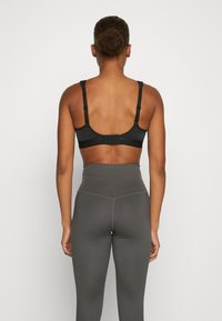 Top sportivo nero con spalline regolabili e chiusura a gancio sul retro, abbinato a leggings grigi a vita alta. Texture liscia.