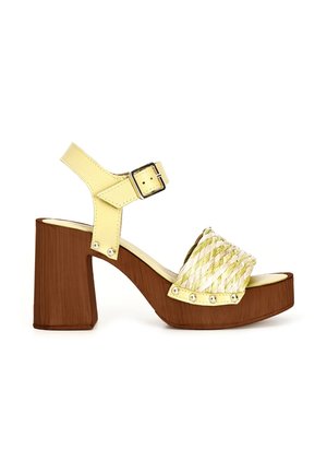 Sandale en cuir jaune avec bride avant tressée, boucle à la cheville, talon bloc en bois et détails cloutés sur les brides latérales.