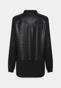 Chemise noire à manches longues ; le dos présente une texture brillante, semblable à du cuir en haut et un tissu mat en dessous. Poignets et col à boutonnière.