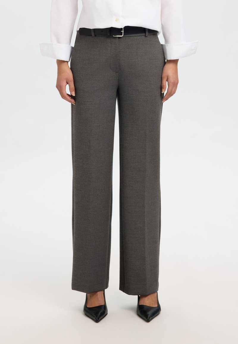 Sivé nohavice s širokými nohavicami, hladkej textúry a záhybom vpredu, doplnené čiernym opaskom, nosené s bielou košeľou na zapínanie na gombíky.