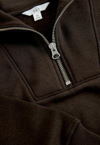 Brun kvart-zip pullover lavet af blødt stof med en sølv lynlås og ribbede manchetter. Etiketten siger "THE SET" i hvid.