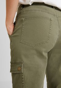 Zielone oliwkowe spodnie cargo o gładkiej teksturze z dwoma tylnymi kieszeniami. Posiadają detal w postaci guzika na kieszeni bocznej.