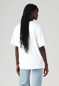 T-shirt blanche surdimensionnée à manches courtes, en coton. Présente un design simple, portée avec un jean décontracté bleu clair.