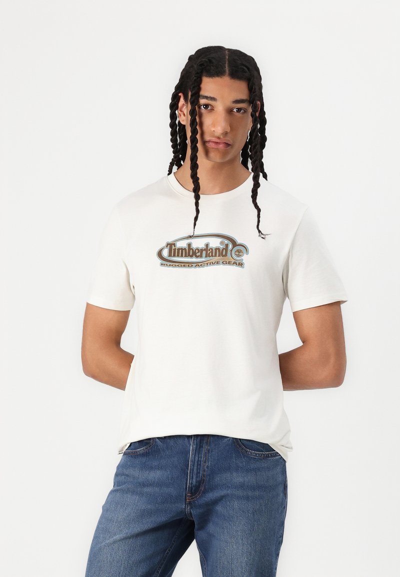 Witte katoenen t-shirt met een blauw en bruin Timberland logo, gestyled met korte mouwen en een ronde hals. Draag het met een blauwe spijkerbroek.