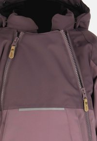 Fioletowa wodoodporna kurtka z wysokim kołnierzem, podwójnymi zamekami z przodu i odblaskowym paskiem. Posiada teksturę materiału oraz złote zamek ozdobne.