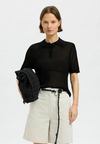 Svart randig polo med korta ärmar och tre knappar, i kombination med ljusbeige shorts och en strukturerad svart meshväska.