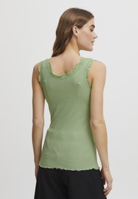 Roheline ribadega tank top, millel on pitsist ääris kaela- ja käeaukude ümber. See on vormikas ja tal on laineline äär.