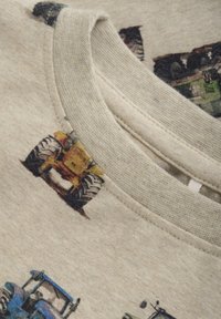 Jasno beżowy sweatshirt z teksturowanym okrągłym dekoltem, z kolorowymi nadrukami ciągników i miękkim, trwałym materiałem.