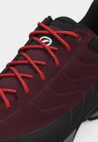 Σκούρο κόκκινο αθλητικό παπούτσι με μαύρες λεπτομέρειες και έντονα κόκκινες κορδόνια με σχέδια, παρουσιάζοντας κοντινή εικόνα των κορδονιών και λεπτομέρειας στο πάνω μέρος του παπουτσιού.