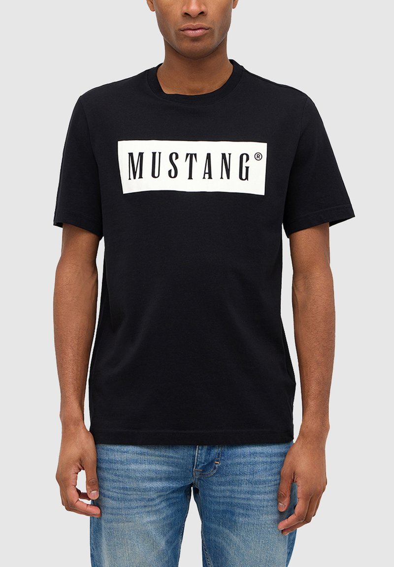 Black cotton t-shirt featuring a white rectangular graphic with the word "MUSTANG" in bold black text, short sleeves, and a crew neckline.