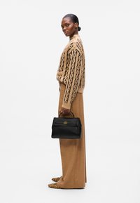 Maglione marrone a maglia con motivo nero, pantaloni beige a vita alta e una borsa nera strutturata con un accento dorato. Scarpe con stampa leopardata.