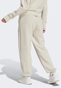 Pantalones de chándal beige hechos de una tela suave, con un corte relajado, puños elásticos y una textura lisa. Combinados con zapatillas deportivas blancas.