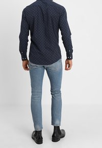 Marinblå mönstrad skjorta med lång ärm och knapp-ner krage, kombinerad med ljusblå skinny jeans och svarta anklarstövlar.