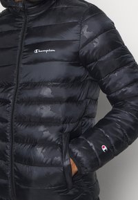 Czarna puchowa kurtka z błyszczącego materiału, z zamkiem błyskawicznym, pikowanym wzorem i subtelnym detalem logo na klatce piersiowej oraz rękawie.