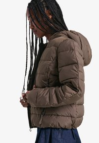 Puhasta jakna v olivno zeleni barvi, s kapuco, kviltano teksturo, z bočnimi žepi in zadrgo.